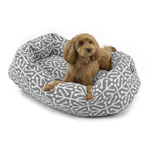 A small brown dog with curly fur lies alert and comfortable on the Majestic Pet Aruba Bagel Dog Bed, which is water resistant, machine washable, features a white bone pattern, and has raised sides for support.