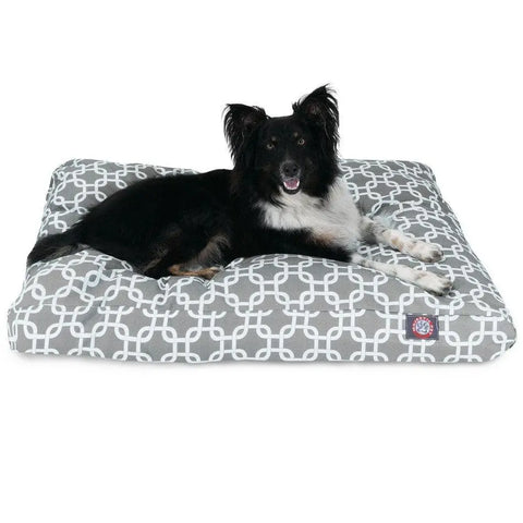 A black and white dog lies on the Majestic Pet Links Memory Foam Dog Bed with a removable cover in a gray and white geometric design, looking forward with its mouth open.