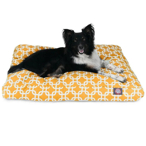 A black and white dog lies comfortably on the Majestic Pet Links Memory Foam Dog Bed, a large yellow bed with a white geometric pattern and a washable, removable cover.