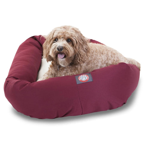 A small, curly-haired brown dog lounges alertly in the maroon Majestic Pet Poly/Cotton Sherpa Bagel Dog Bed with a white interior. This cozy, machine-washable bed keeps your pup comfortable and cleaning easy.