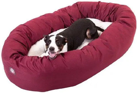 A black and white dog lies happily on a large, oval Majestic Pet Poly/Cotton Sherpa Bagel Dog Bed. The cozy maroon bed is machine washable for easy cleaning.