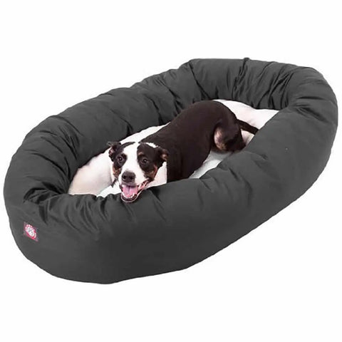 A black and white dog relaxes in a large Majestic Pet Poly/Cotton Sherpa Bagel Dog Bed, which is oval-shaped and water resistant, looking up with its mouth open and tongue out.