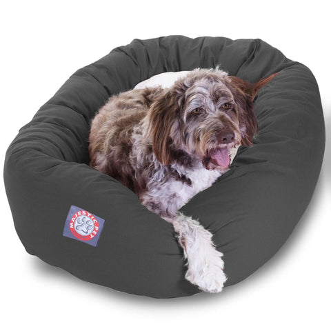 A fluffy brown and white dog is relaxing with its tongue out on the Majestic Pet Poly/Cotton Sherpa Bagel Dog Bed, which features a water-resistant base, comfy Sherpa cushion, and a paw print logo.
