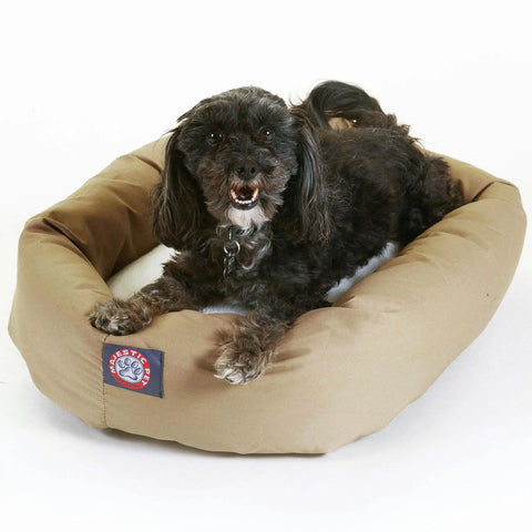 A small, fluffy black dog lies on a Majestic Pet Poly/Cotton Sherpa Bagel Dog Bed with a soft tan cushion, posing on a white background.