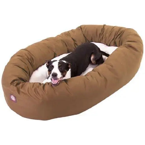 A black and white dog relaxes on a Poly/Cotton Sherpa bagel bed by Majestic Pet, inside an oval, water-resistant brown bed, looking up with its mouth open and tongue out.