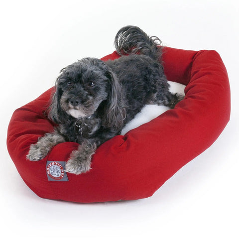 A small black and gray dog with curly fur rests on a red Majestic Pet Poly/Cotton Sherpa Bagel Dog Bed with a cozy sherpa cushion, shown against a white background.