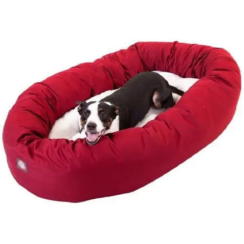 A content black and white dog lounges in a large, oval Majestic Pet Poly/Cotton Sherpa Bagel Dog Bed with a plush cushion and water-resistant materials for extra comfort.
