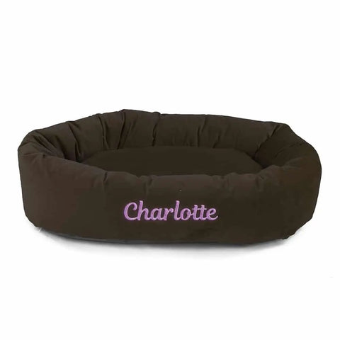 The Majestic Pet Velvet Bagel Dog Bed - Personalized is a brown oval bed with Charlotte embroidered in light purple. It features raised sides, a soft cushioned interior, and offers gentle spine support for your pets comfort.