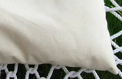 A close-up of a cream-colored Cobble Mountain Replacement Pillow resting on a white rope hammock above green grass—ideal for anyone looking for American-made outdoor cushions for their backyard oasis.