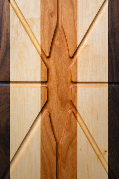 The Oval Carver by Montana Block is a handmade solid wood cutting board from Montana, featuring geometric carved patterns and contrasting vertical stripes of light and dark wood.