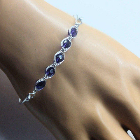 The Alexa Martha Designs Larger Oval Shaped Swarovski Crystal Bar Bangle Bracelet, featuring five purple crystals in wire-wrapped bezels, is shown on a mannequin hand. Fits an 8 inch wrist. Displayed against a plain light background.