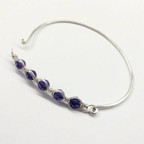 The Larger Oval Shaped Swarovski Crystal Bar Bangle Bracelet by Alexa Martha Designs features five faceted dark purple crystals, wire-wrapped in sterling silver. Perfect for 8-inch wrists, it adds elegant sparkle to any outfit.