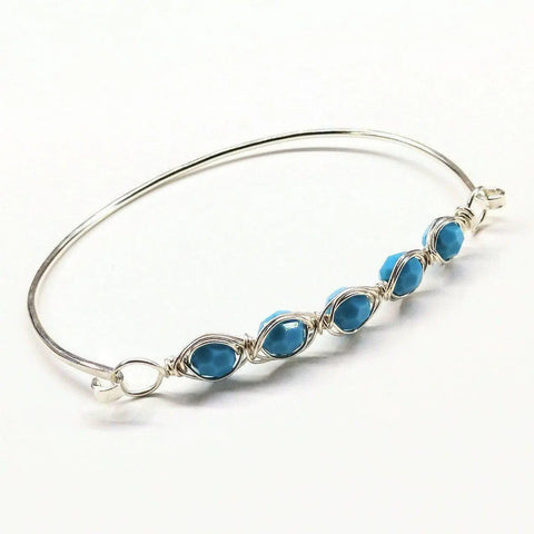 The Larger Oval Shaped Swarovski Crystal Bar Bangle Bracelet by Alexa Martha Designs features five blue Swarovski crystals in wire-wrapped settings, evenly spaced along a sterling silver bangle for an elegant and eye-catching look.