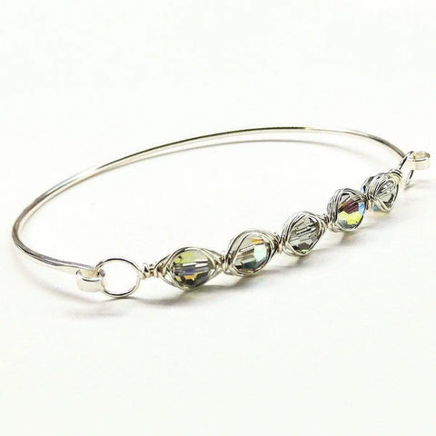 The Larger Oval Shaped Swarovski Crystal Bar Bangle Bracelet by Alexa Martha Designs features five iridescent faceted beads, each intricately wire wrapped in sterling silver, elegantly displayed on a plain white background.