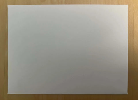 A blank sheet awaits on a light wood surface, ready to become a JuLu Cards Pack of 4 - Cardinal on Branch (20074) watercolor greeting card. Photographed from above, the paper is pristine and unmarked.