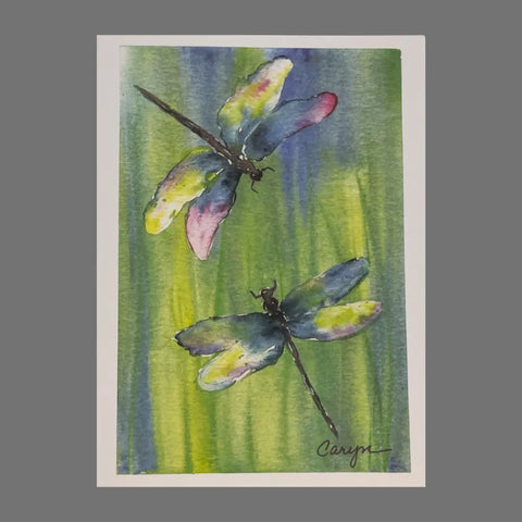 Pack of 4 JuLu Cards – “Two Dragonflies Over Blue and Green” (20047) features watercolor dragonflies with blue, green, and pink wings on a soft background. Each 4.5 x 6.25 card includes an envelope; artwork is signed Caryn bottom right.