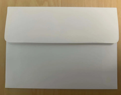 A white envelope with flap closed, on a light wooden surface—ideal for sending JuLu Cards Pack of 4 Thinking of You With Colorful Flowers (20072) greeting cards.