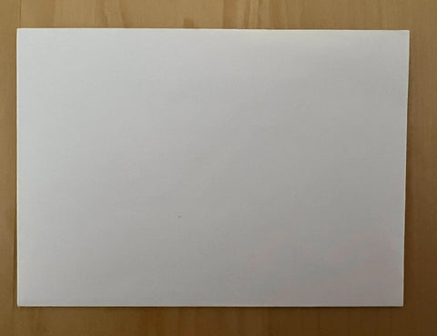 A blank white sheet rests on a light brown wooden surface, ready to become a JuLu Cards Pack of 8 - Pink Roses (10112) greeting card. The clean, centered paper awaits your creative touch.