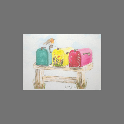 JuLu Cards’ Pack of 8 - Three Colorful Mailboxes (10111) features green, yellow floral, and pink mailboxes on a wooden stand outdoors with a bird atop the green one—vividly illustrated against blue sky and grass for perfect greeting cards.