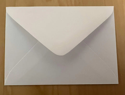 A white envelope with its flap closed rests on a light wooden surface, ready to hold your JuLu Cards Pack of 8 - Sailboats on the Lake (10108) coastal greeting card.