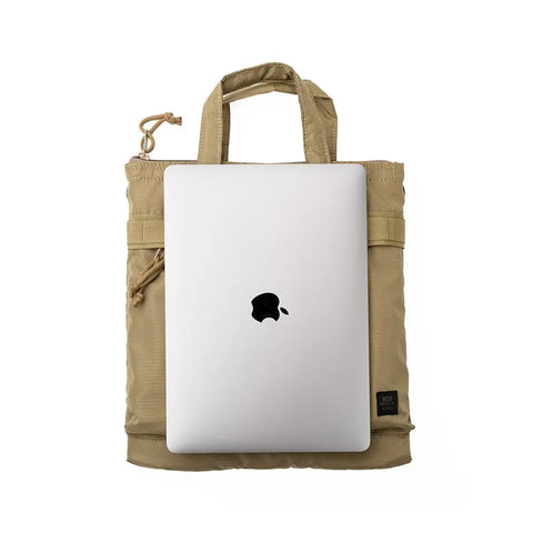 A silver laptop with a black Apple logo is partially inserted into an MIS Padded F Helmet Bag S in Coyote Tan, made of packcloth nylon with short handles, a zipper pocket, and padded main compartment. Made in USA. Shown on white background.