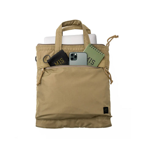 The MIS Padded F Helmet Bag S in Coyote Tan, made from packcloth nylon, features a padded main compartment holding a laptop, smartphone, black wallet, green notebook, and keychain—partially visible in the main section and front zipper pocket.