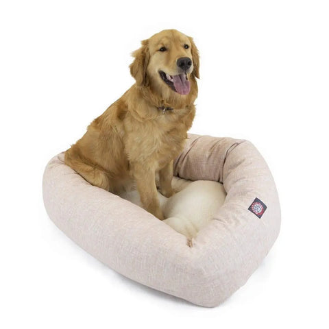 A golden retriever relaxes on the Majestic Pet Palette Heathered Sherpa Bagel Dog Bed, a light beige bed with raised sides for spine support. The dog looks content, mouth open and tongue out, enjoying the cozy, machine washable bed.