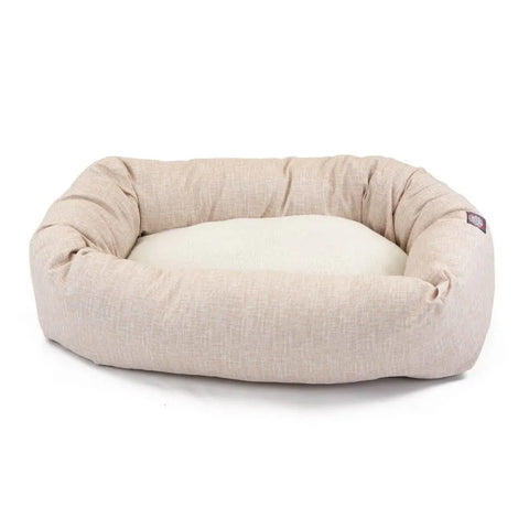 The Majestic Pet Palette Heathered Sherpa Bagel Dog Bed features raised, cushioned sides for spine support and a soft, cream-colored interior. Light beige and machine washable, it’s shown on a white background.