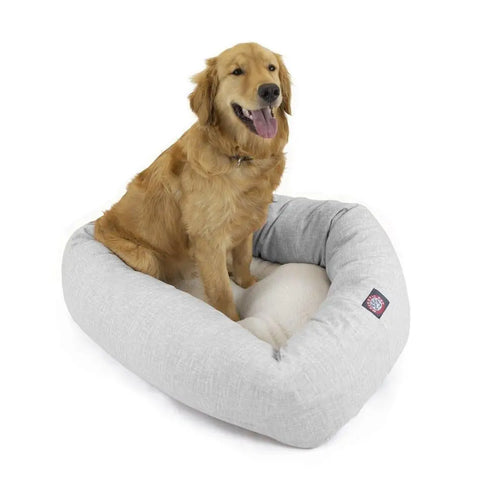 A golden retriever sits happily in a Majestic Pet Palette Heathered Sherpa Bagel Dog Bed, featuring a light gray color, soft interior, spine support, and a small label on the side.