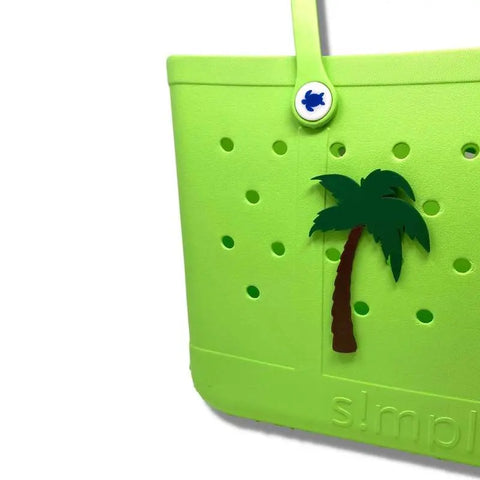 A bright green Simply Southern bag by Chatelet Manufacturing, featuring a Boglets BEACH palm tree charm and blue fish button, with circular holes for accessories and simpl embossed near the bottom.