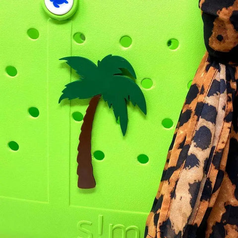 Add a fun touch to your Simply Southern Bags with the Chatelet Manufacturing BOGLETS Palm Tree Charm—green and brown palm tree decor on a vibrant green base, perfect for accessorizing bags or other accessories.