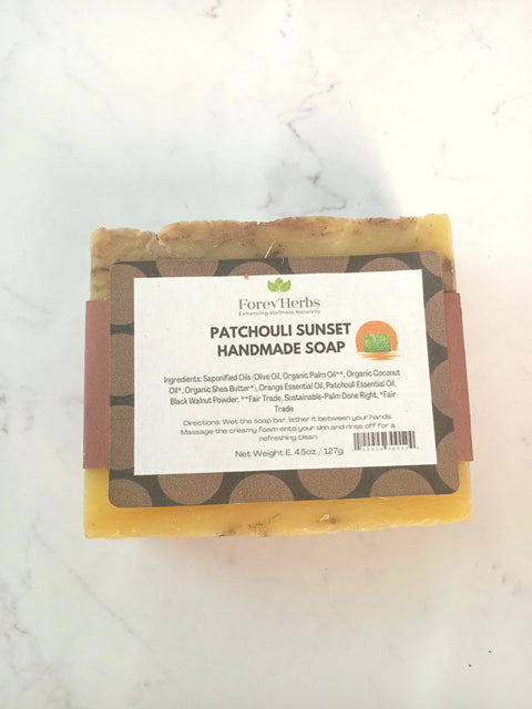 A bar of Forev'Herbs Patchouli Sunset Handmade Soap, a natural men’s soap with brown and yellow layers and a detailed ingredient label, rests on a white marble surface.
