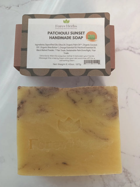 A rectangular bar of Patchouli Sunset Handmade Soap by Forev'Herbs sits on marble, with its brown and white label showing ingredients and usage instructions above this natural men's soap.