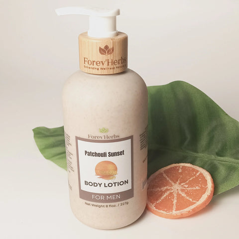 A bottle of Forev'Herbs Patchouli Sunset Lotion rests on a green leaf beside sliced grapefruit, set against a white background. The bottle has a wooden pump and a beige label.