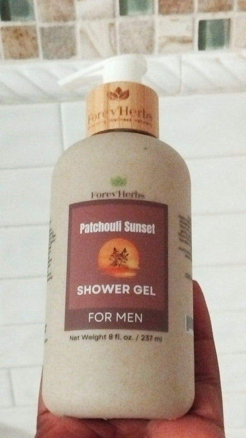 A hand holds a bottle of Forev'Herbs Patchouli Sunset Shower Gel with a beige label and wooden cap, set against white bathroom tiles. The bottle contains 8 fl. oz. (237 ml).