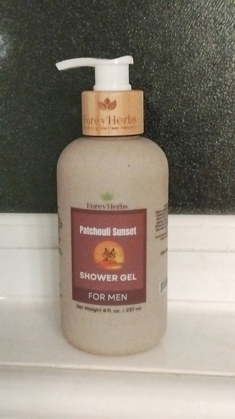 A bottle of Forev'Herbs Patchouli Sunset Shower Gel with a pump dispenser rests on a white surface in front of a dark textured window.