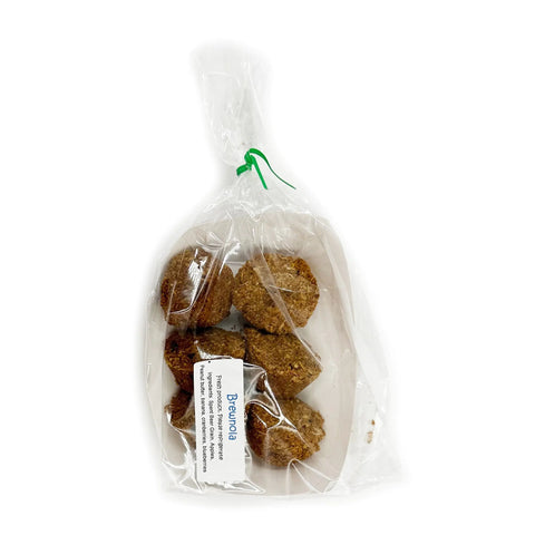 A clear plastic bag tied with a green twist holds several brown, round Brewnola dog treats by Brewscuits, made from spent beer grains. A white label with black text is attached to the bag. The background is plain white.
