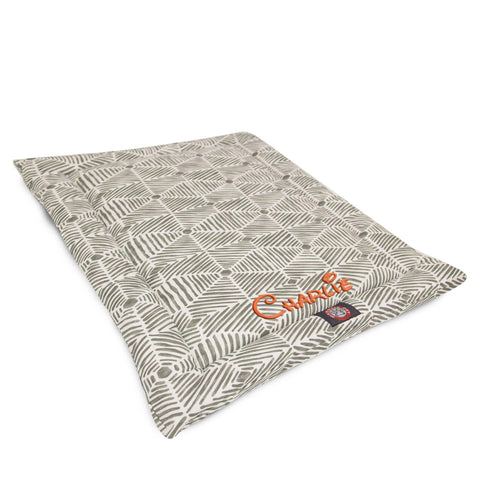The Majestic Pet Charlie Crate Mat - Personalized features gray leaf patterns on white, an orange-embroidered name Charlie, and is machine washable—adding comfort and style to your dogs space.