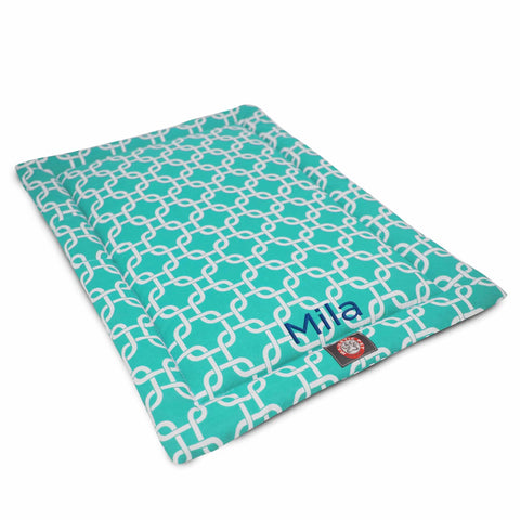 The Majestic Pet Links Crate Mat - Personalized is a rectangular teal polyester dog mat with a white geometric chain pattern, the name Mila, and a small red paw print tag near one corner.