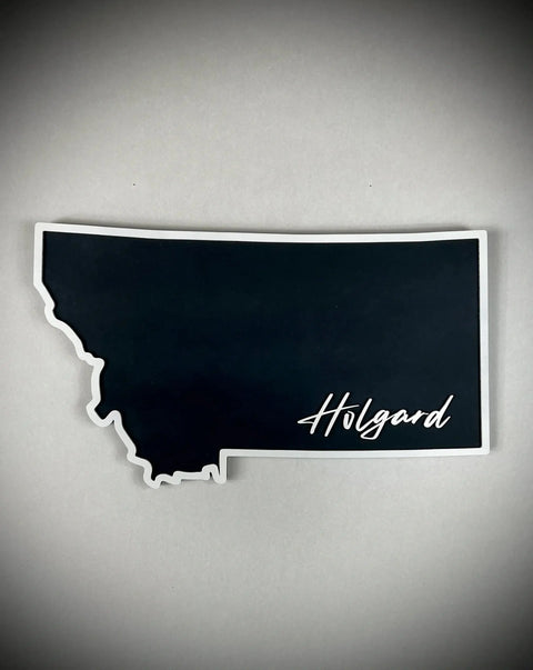 The Medium Floating MT Outline Sign Personalized by B. James Design & Woodwork features a black Montana-shaped sign with Holgard in white script at the bottom right—ideal as a unique home decor piece or custom sign.