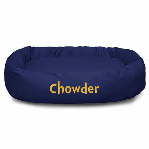 A navy blue Majestic Pet Poly/Cotton Bagel Bed - Personalized, embroidered with Chowder in yellow on the front, offers spine support and is fully machine washable for easy care.