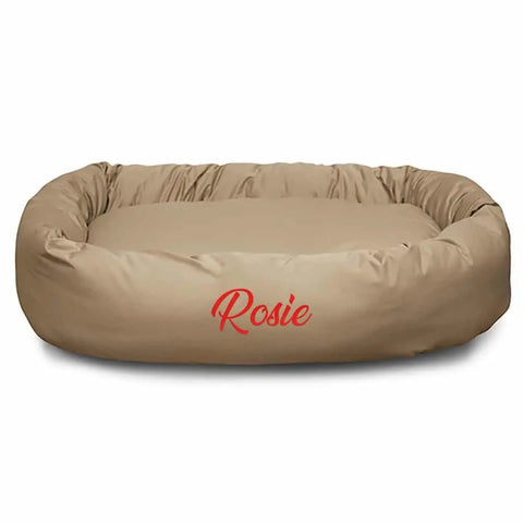 A tan, oval Majestic Pet Poly/Cotton Bagel Bed with raised sides for spine support, personalized with “Rosie” embroidered in red on the front.