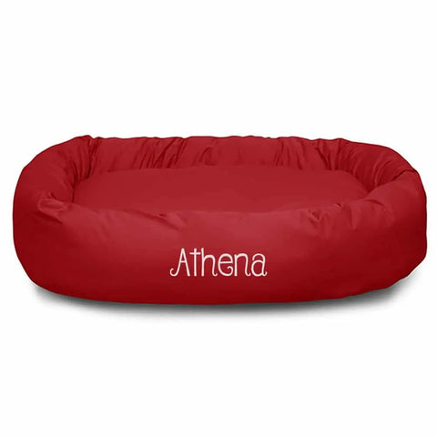 A red, oval-shaped Poly/Cotton Bagel Bed - Personalized by Majestic Pet, featuring Athena in white letters on the front. It has raised sides and a soft cushioned base to provide ultimate comfort for your pet.