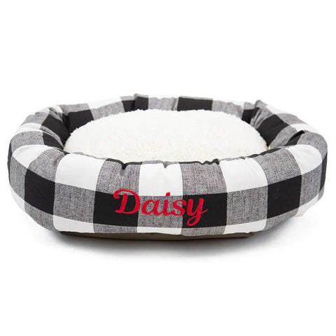 The Majestic Pet Anderson Check Sherpa Bagel Bed features a black and white plaid pattern, soft white cushion for spine support, and can be personalized with Daisy embroidered in red on the front.