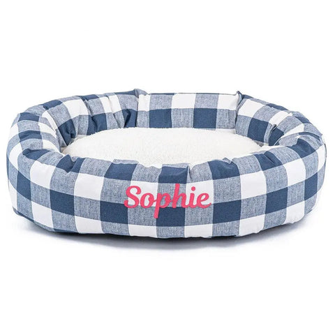 The Anderson Check Sherpa Bagel Bed by Majestic Pet features a blue and white checkered pattern, soft white cushion for spine support, and can be personalized with your pet’s name embroidered on the front.