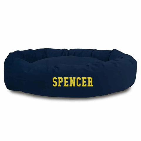 The Majestic Pet Suede Bagel Dog Bed is a round, navy blue suede bed with a removable slipcover and “SPENCER” embroidered in large yellow letters on the front.
