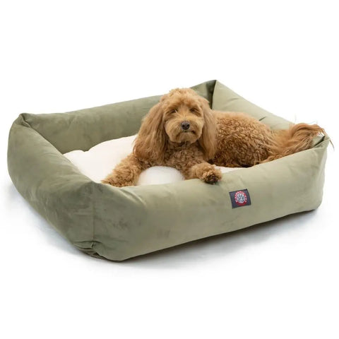 A small, curly-haired brown dog lounges in a Majestic Pet Suede Luxe Bagel Bed – Personalized, featuring a green rectangular design and a soft white cushion filled with plush fiberfill.