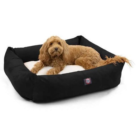 A fluffy, light brown dog lounges on the Majestic Pet Suede Luxe Bagel Bed – Personalized, featuring a plush fiberfill cushion and a black, machine-washable slipcover.