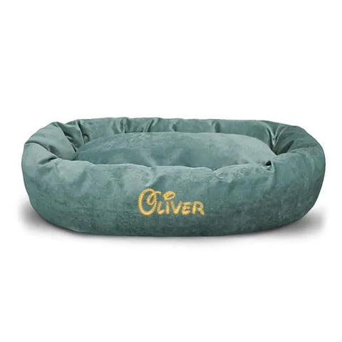 The Majestic Pet Villa Bagel Dog Bed - Personalized is a soft, oval teal bed made from water-resistant polyester micro-velvet, featuring Oliver embroidered in yellow on the side.