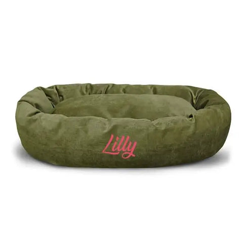 The Majestic Pet Villa Bagel Dog Bed is an oval, olive green, water-resistant micro-velvet bed with Lilly embroidered in pink on the front.